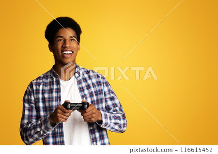 Gambling Addiction. Excited Guy Holding Joystick and Playing Video Games, Yellow Background 116615452