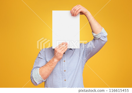 A man holding a blank white piece of paper over his face in the air against a plain yellow studio background, mockup, copy space A man holding a blank white piece of paper over his face in the air against a plain yellow studio background, mockup, copy space 116615455