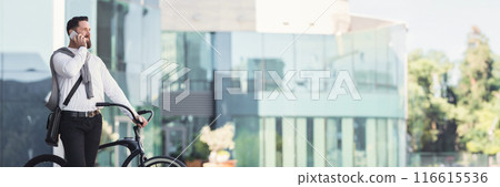 Smiling businessman talking over mobile phone standing on street with his bicycle, panorama with copy space Smiling businessman talking over mobile phone standing on street with his bicycle, panorama with copy space 116615536