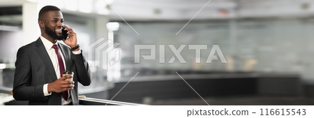 Cheerful young black bearded man manager standing at office building corridor, drinking coffee to go, having phone conversation with business partner and smiling, panorama with copy space 116615543