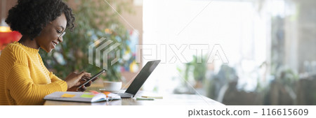 Happy young black lady freelancer using mobile phone, working with laptop in cafe, side view, panorama with copy space Happy young black lady freelancer using mobile phone, working with laptop in cafe, side view, panorama with copy space 116615609