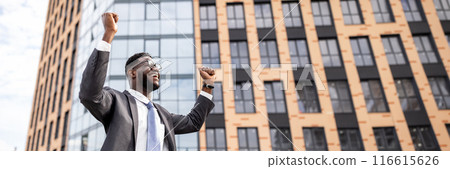 Excited african american businessman celebrating success and raising hands up, going from business meeting and standing outdoors near modern office center, empty space Excited african american businessman celebrating success and raising hands up, going from business meeting and standing outdoors near modern office center, empty space 116615626