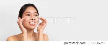 Skincare Concept. Portrait of positive Asian woman touching healthy facial skin. Beautiful smiling lady with natural makeup applying cream on hydrated skin on white studio background, copy space Skincare Concept. Portrait of positive Asian woman touching healthy facial skin. Beautiful smiling lady with natural makeup applying cream on hydrated skin on white studio background, copy space 116615749