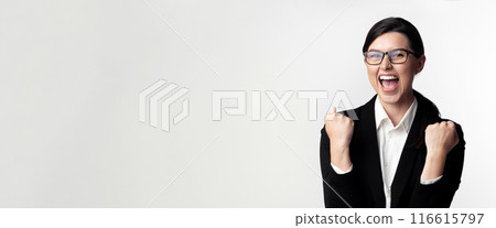 A young woman in a black suit and glasses is celebrating success with a clenched fist and a big smile. A young woman in a black suit and glasses is celebrating success with a clenched fist and a big smile. 116615797