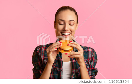 Cheat Meal. Joyful Young Woman Eating Burger Standing In Studio On Yellow Background. Cheat Meal. Joyful Young Woman Eating Burger Standing In Studio On Yellow Background. 116615894