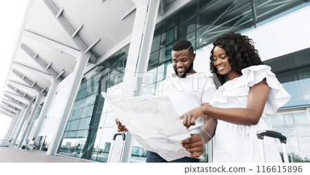 African American couple stands outside a modern airport, looking at a map together. They are both smiling and seem excited about their trip, copy space 116615896