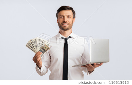 A smiling man in a white shirt and tie holds a fan of cash in one hand and a laptop in the other, against a white background. A smiling man in a white shirt and tie holds a fan of cash in one hand and a laptop in the other, against a white background. 116615913