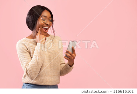 Excited African American Girl Using Smartphone Holding Finger On Chin Standing Over Pink Studio Background. Empty Space 116616101