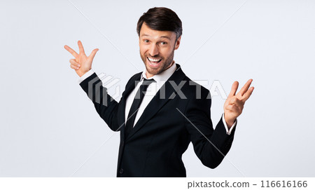 A businessman in a black suit smiles and gestures with both hands against a white background. 116616166