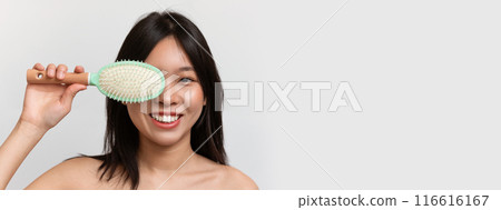 Happy japanese lady holding hair brush, covering eye and smiling at camera, posing over white background, panorama. Young woman with beautiful dark hair enjoying her new hair brush, copy space 116616167