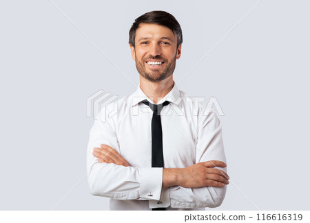 Cheerful Business Guy Smiling At Camera Crossing Hands Standing Over White Studio Background. Isolated, Empty Space 116616319