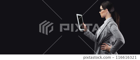 A woman in a gray blazer uses a tablet computer against a black background. 116616321
