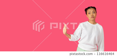 Asian young woman standing in front of a bright pink background. She is looking to the right, with a serious expression on her face. Her right arm is extended out in front of her, copy space Asian young woman standing in front of a bright pink background. She is looking to the right, with a serious expression on her face. Her right arm is extended out in front of her, copy space 116616464