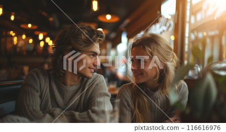 A young couple sits at a table in a cafe, looking lovingly into each other's eyes. 116616976