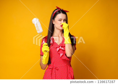 Young woman with toilet brush in gloved hands on orange background Young woman with toilet brush in gloved hands on orange background 116617287