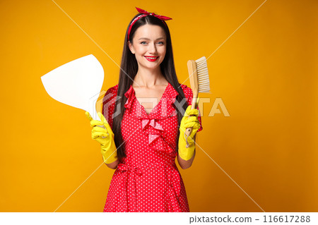 Smiling young woman with brush and dustpan in hands on orange background 116617288