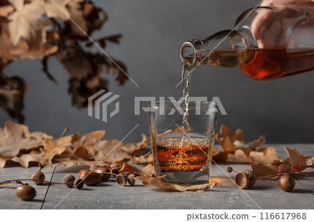 Whiskey on a grey stone table with dried-up oak leaves. 116617968