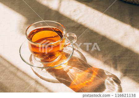 A cup of tea in glass cup and saucer illuminated by warm sunlight on a light table. Horizontal frame, copy space A cup of tea in glass cup and saucer illuminated by warm sunlight on a light table. Horizontal frame, copy space 116621138