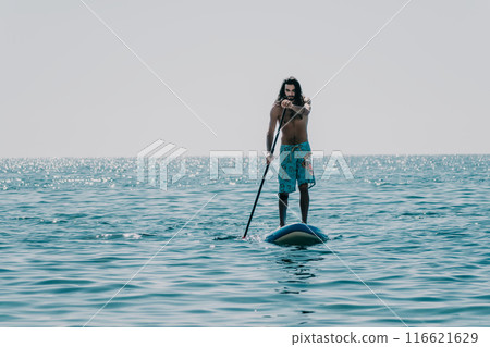 Man Sup Sea. Strong athletic man learns to paddle sup standing on board in open sea ocean on sunny day. Summer holiday vacation and travel concept. Aerial view. Slow motion 116621629