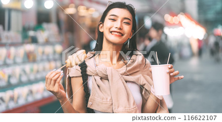 Happy asian foodie woman eating street food holding korea skewer oden 116622107