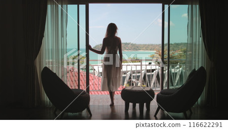 Woman elegance walking on balcony, enjoy ocean view from hotel room apartment, sunny day. Outdoor lifestyle travel on summer holiday vacation. Phuket tropical island, Thailand. Back view Woman elegance walking on balcony, enjoy ocean view from hotel room apartment, sunny day. Outdoor lifestyle travel on summer holiday vacation. Phuket tropical island, Thailand. Back view 116622291