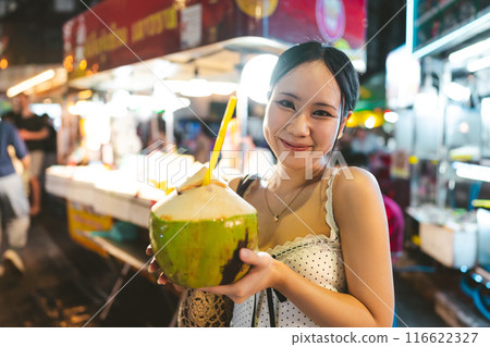 Asian tourist woman eating coconut juicetraveling at China town asia street food night market Asian tourist woman eating coconut juicetraveling at China town asia street food night market 116622327
