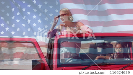 Image of flag of usa over african american and caucasian female friends sitting in car 116624629