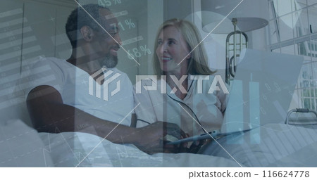 Image of infographic interface moving over happy diverse couple using laptop on bed at home 116624778