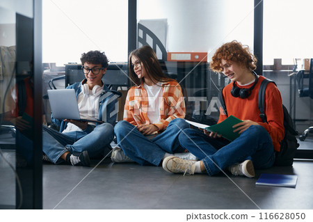 Three teenagers sitting on floor and discussing actual work topics Three teenagers sitting on floor and discussing actual work topics 116628050