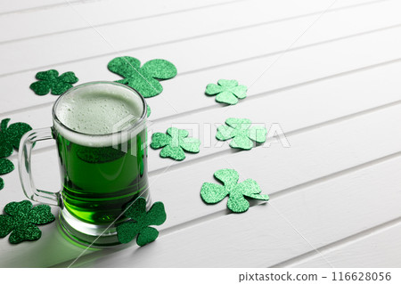 Image of glass with green beer, clover and copy space on white wooden background 116628056