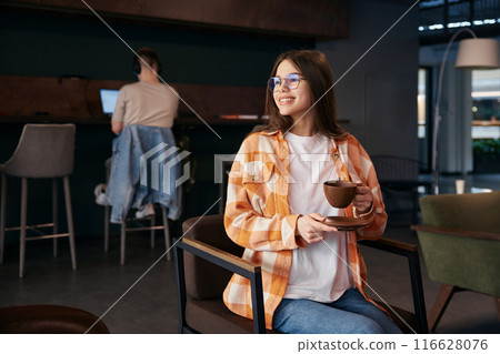 Pretty teenage girl resting on chair, drinking coffee Pretty teenage girl resting on chair, drinking coffee 116628076