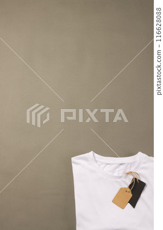 A white t-shirt with a blank tag lies on a plain background, with copy space 116628088