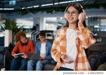 Smiling teenage girl listening music in comfortable modern place 116628093