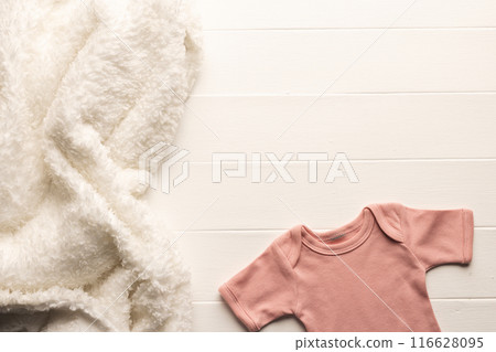 Cozy blanket and onesie on wood evoke newborn warmth and preparation. Cozy blanket and onesie on wood evoke newborn warmth and preparation. 116628095