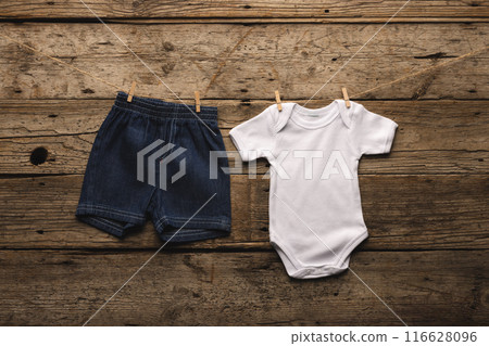 Baby denim shorts and onesie on a clothesline evoke childhood innocence. 116628096