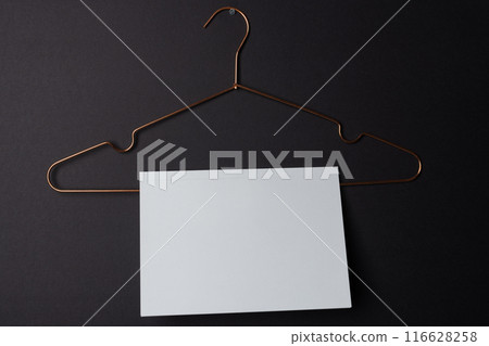 A blank white card hangs on a copper hanger against a dark background with copy space A blank white card hangs on a copper hanger against a dark background with copy space 116628258