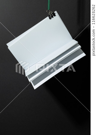 Blank white paper sheets hang from a clip against a black background, with copy space Blank white paper sheets hang from a clip against a black background, with copy space 116628262