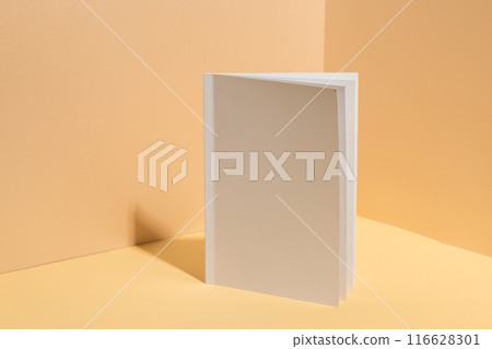 A blank white book stands open against a beige background with copy space 116628301