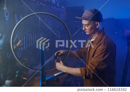 Repairman doing tensioning and alignment of bicycle spokes closeup view 116628382
