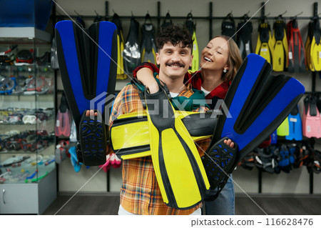 Young joyful man and woman couple holding diving flippers while shopping at sport store 116628476