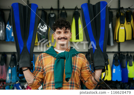 Portrait of hipster man holding flippers posing for camera over sportive shop 116628479