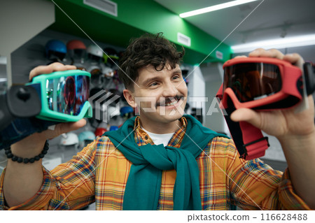 Closeup face portrait of man buyer choosing between two goggles mask Closeup face portrait of man buyer choosing between two goggles mask 116628488