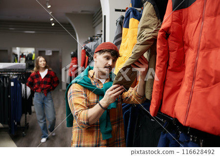 Man customer choosing sportive outwear at fashion sports clothing boutique. Man customer choosing sportive outwear at fashion sports clothing boutique. 116628492