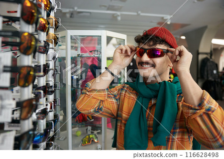Young hipster man choosing trendy sunglasses at sports shop 116628498