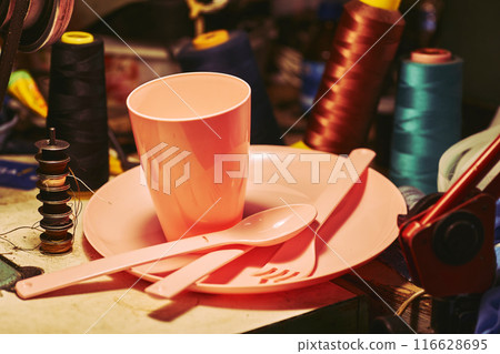 Orange plastic dinnerware set in tailor sewing workshop.Cup,fork,knife,spoon Orange plastic dinnerware set in tailor sewing workshop.Cup,fork,knife,spoon 116628695