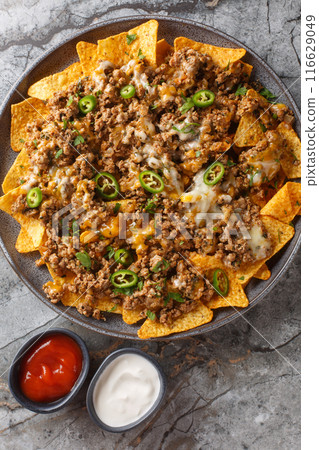 Cheesy Beef Nachos Tortilla chips covered with seasoned ground beef and melted cheese closeup on the plate. Vertical top view Cheesy Beef Nachos Tortilla chips covered with seasoned ground beef and melted cheese closeup on the plate. Vertical top view 116629049