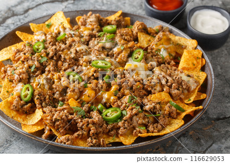 Corn nachos with lots of stewed minced meat, cheddar cheese and jalapeno  pepper served with sauces closeup on the plate. Horizontal 116629053