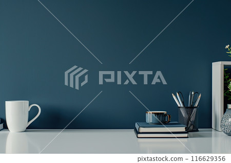 Dark blue wall and home office desk with supplies, pencils, ceramic coffee mug, box, plant vase. Creative stylish minimal workspace. Contemporary white wood work tabletop for products display montage 116629356