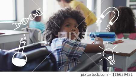 Image of science icons over happy biracial schoolboy in wheelchair at desk in class 116629451