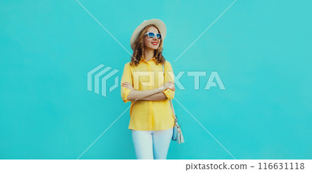Beautiful young woman with crossed arms looking away in summer tourist hat on blue background 116631118